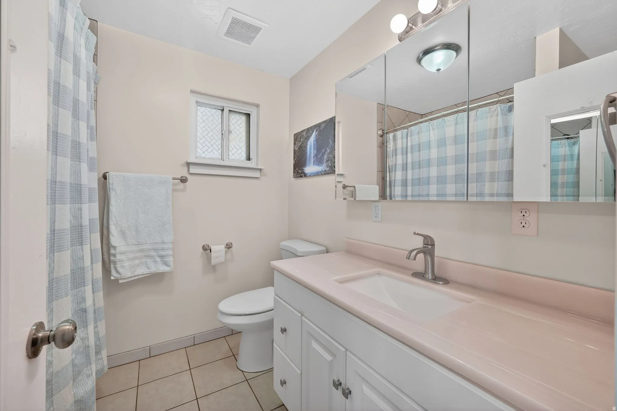 Bathroom featuring a white vanity with a pink countertop and integrated sink, brushed nickel faucet, and a large mirrored medicine cabinet