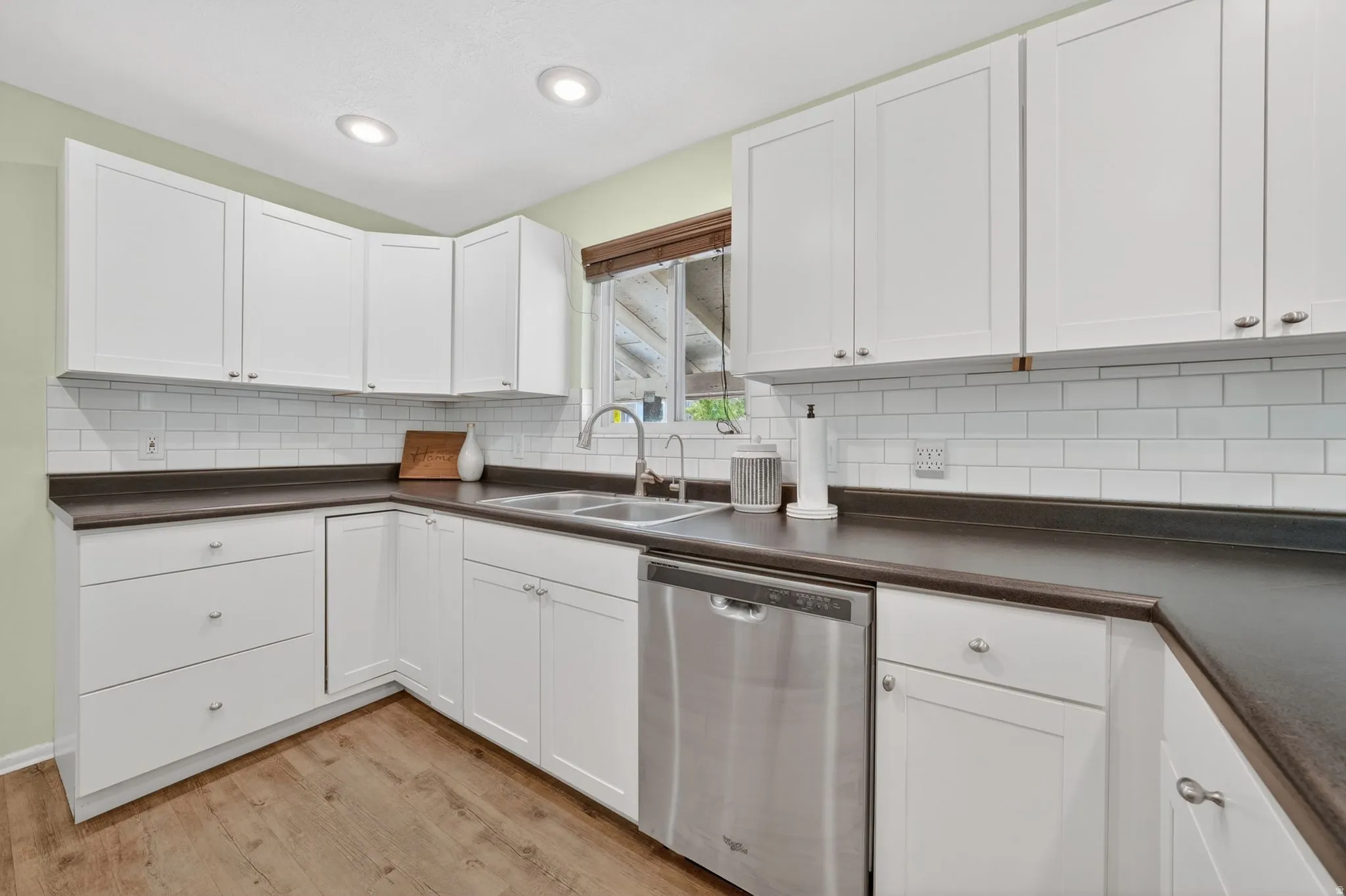 White shaker-style cabinetry with dark countertops, a stainless steel dishwasher, and a double basin sink