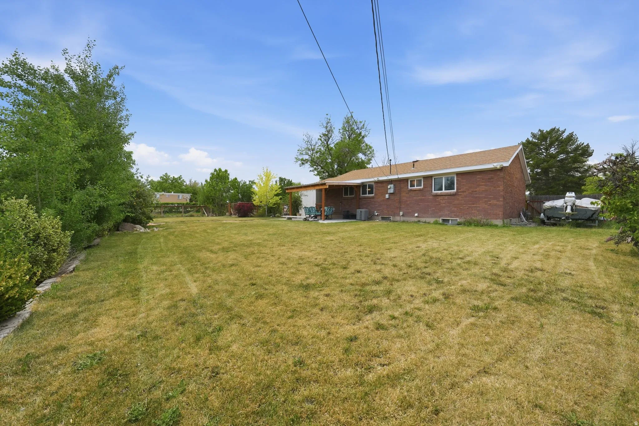Expansive backyard featuring a brick exterior structure, a covered patio area, multiple windows, and mature perimeter trees