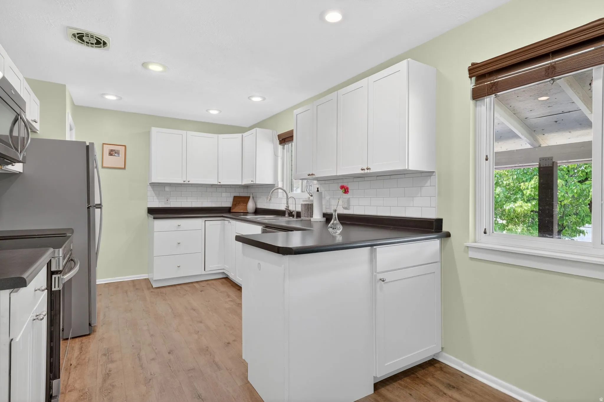 Kitchen featuring white cabinetry, dark countertops, a white subway tile backsplash, stainless steel appliances, and wood-finish flooring
