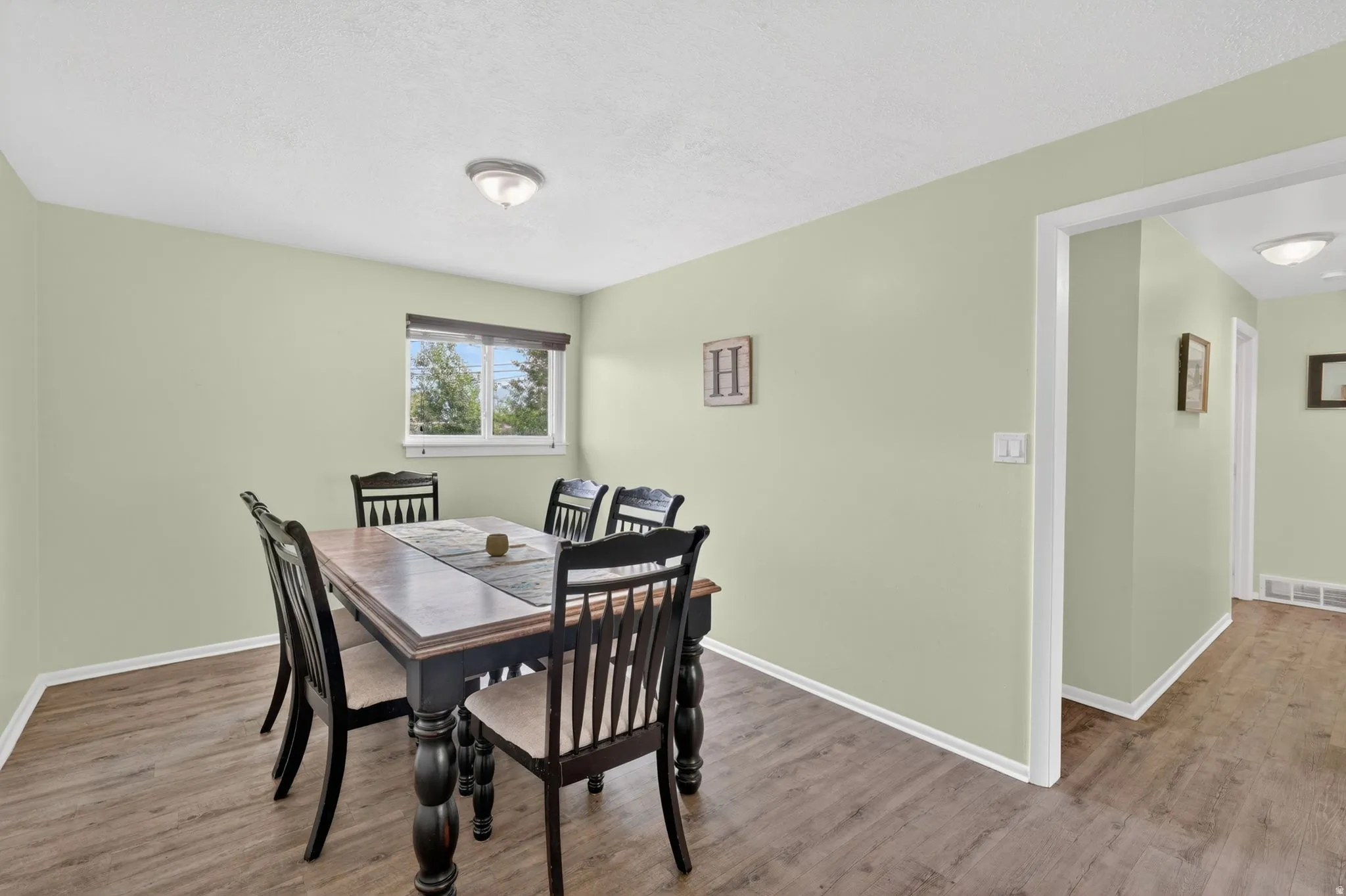 Wood-finish flooring extending from the entry into the room, light green walls, a window with a brown blind, white trim, and a flush mount ceiling light