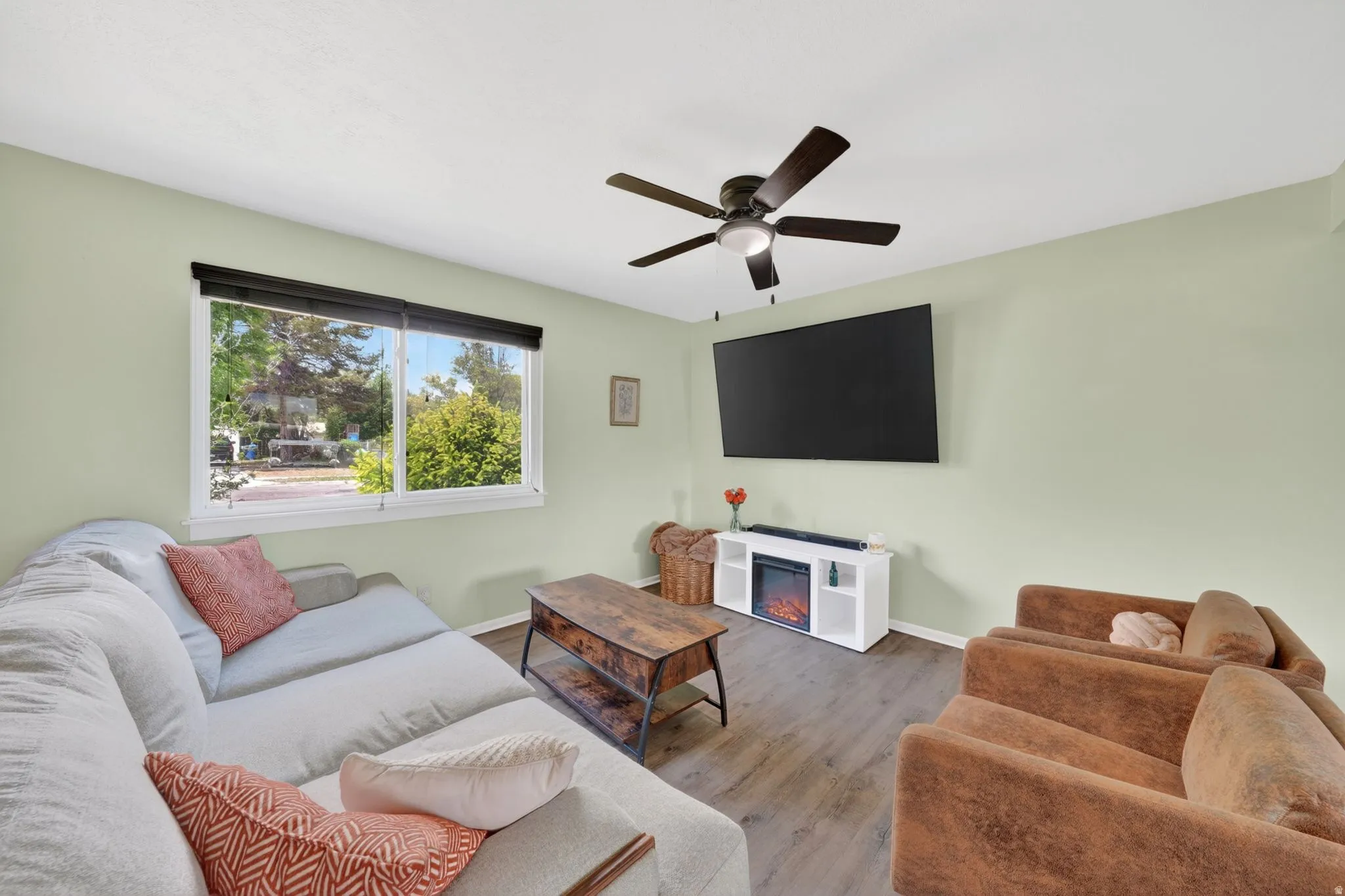 Open living area featuring wood-finish flooring, a contemporary ceiling fan with integrated lighting, and a large window