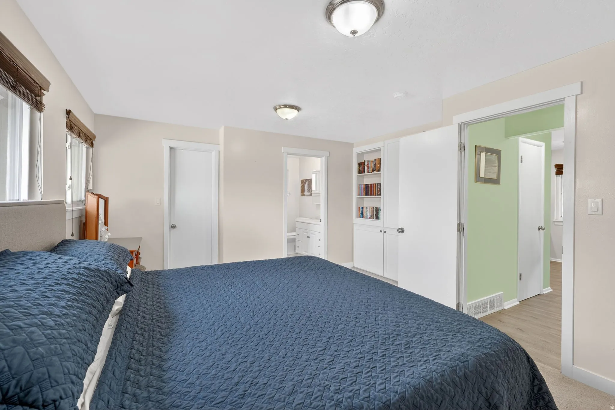 Bedroom featuring two windows with wood-finish blinds, built-in white cabinetry with open shelving and closed storage, and a ceiling-mounted light fixture