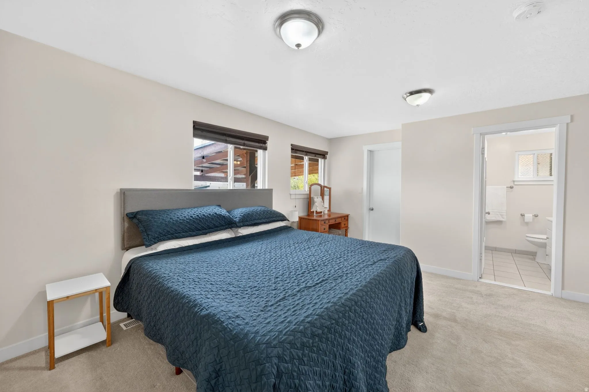 Carpeted bedroom featuring an upholstered headboard, dual windows with blinds, and flush mount lighting