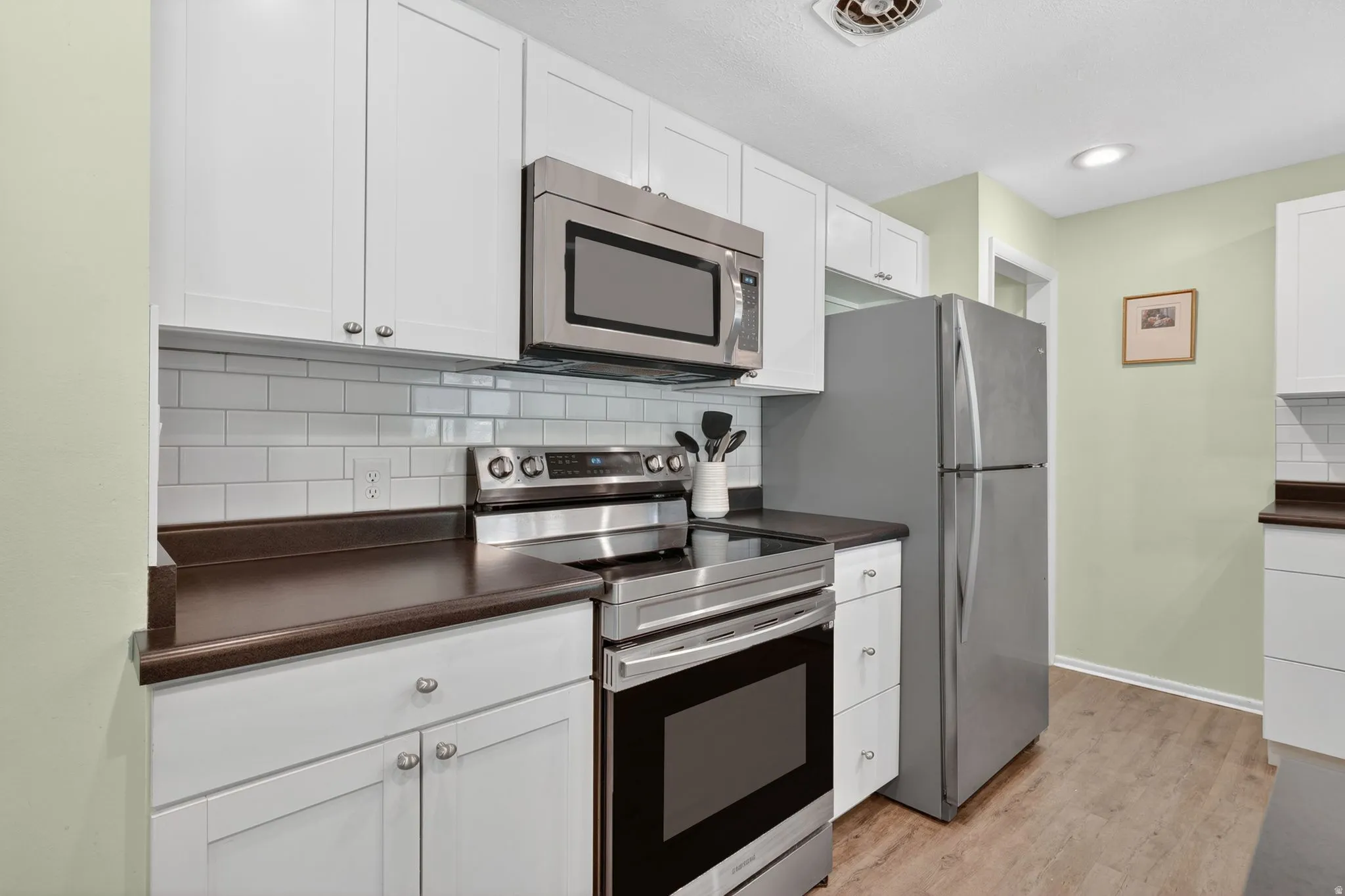 Kitchen featuring stainless steel appliances, white shaker-style cabinetry, and wood-finish flooring