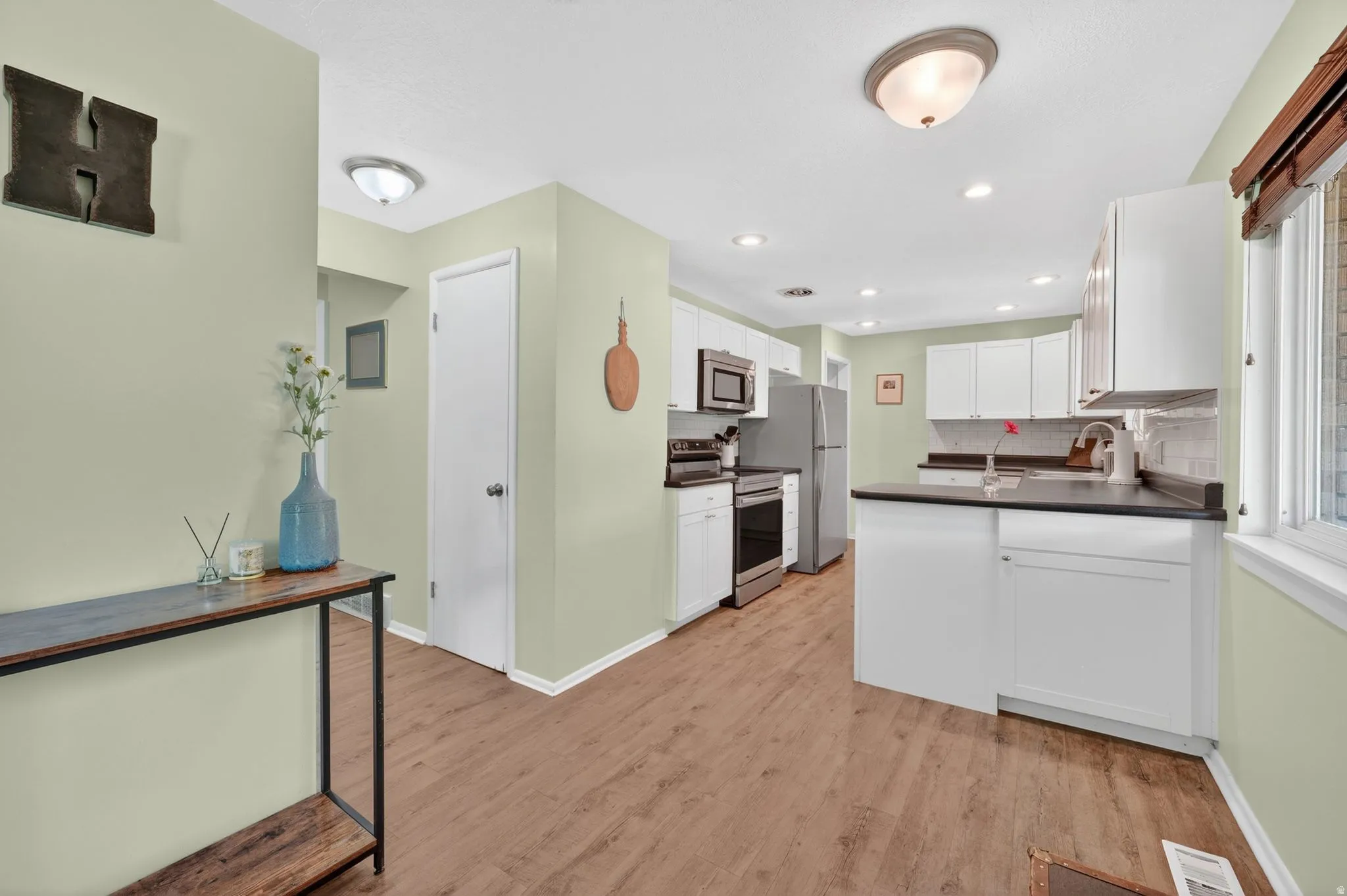 Bright kitchen featuring white cabinetry, dark countertops, a stainless steel refrigerator, and wood-finish flooring