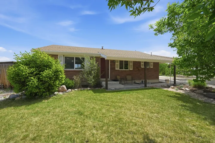 Brick exterior with a covered patio, landscaped front yard, mature trees, and a gravel side yard