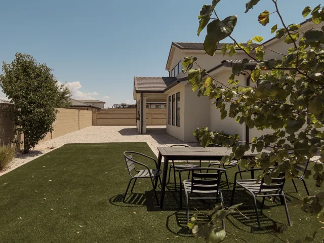 Expansive backyard featuring artificial turf, gravel landscaping, a mature tree, perimeter block fencing, and a stucco exterior with dark trim
