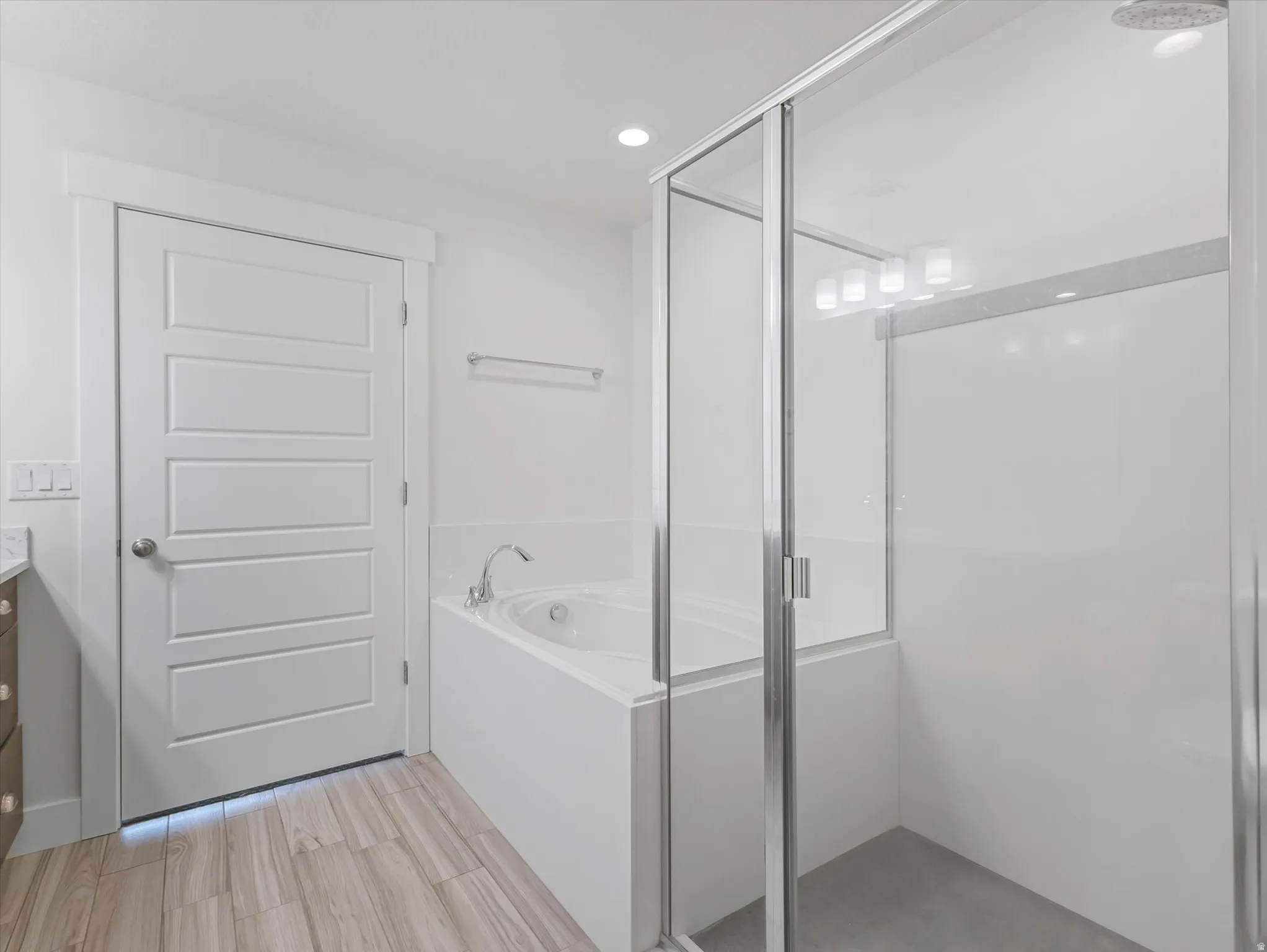 Contemporary bathroom featuring a built-in soaking tub with deck-mounted faucet, an enclosed glass shower, and wood-finish tile flooring