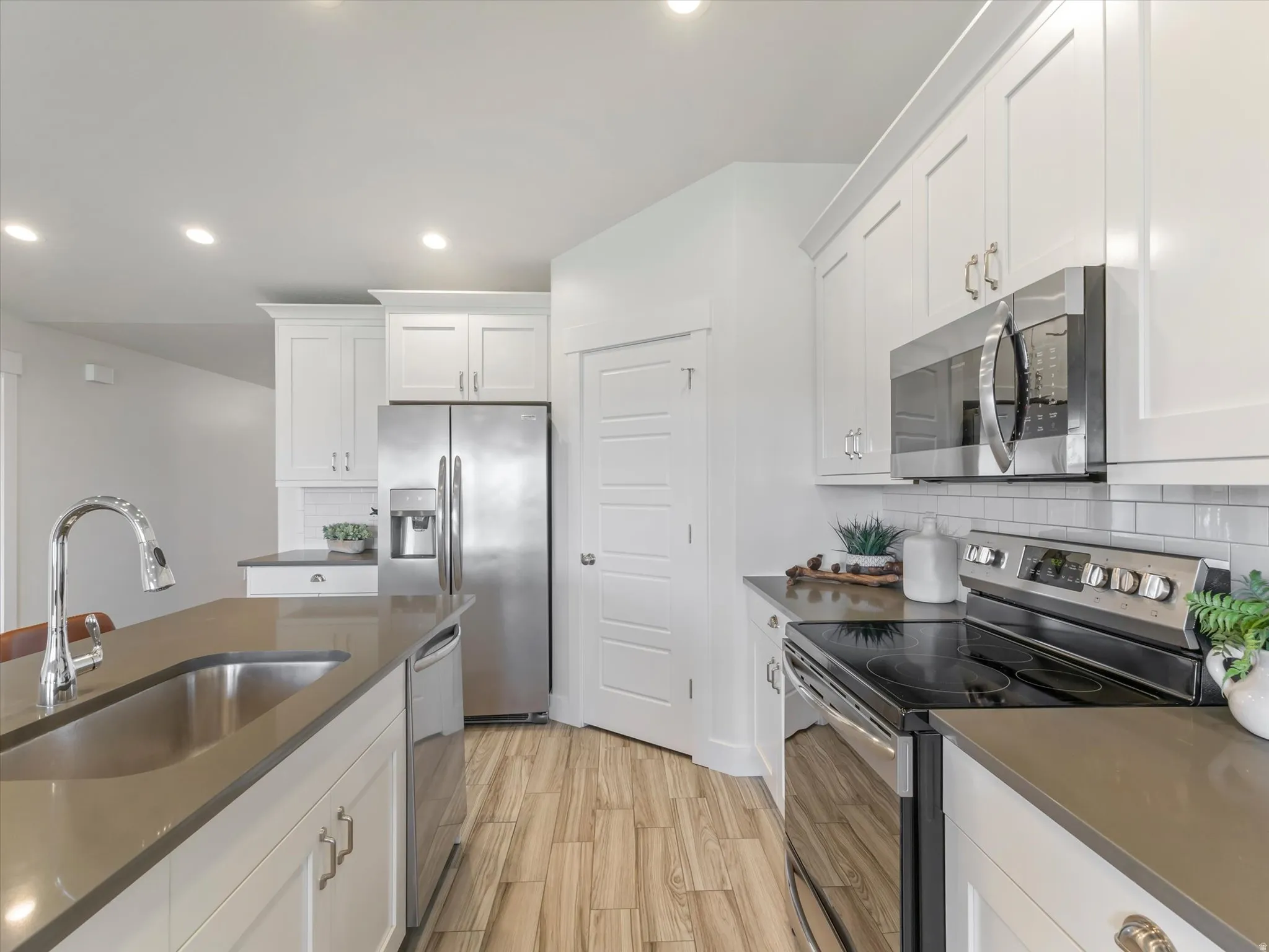 Modern kitchen featuring a large island with an undermount sink, stainless steel appliances, white shaker cabinetry, light-colored countertops, and wood-finish flooring