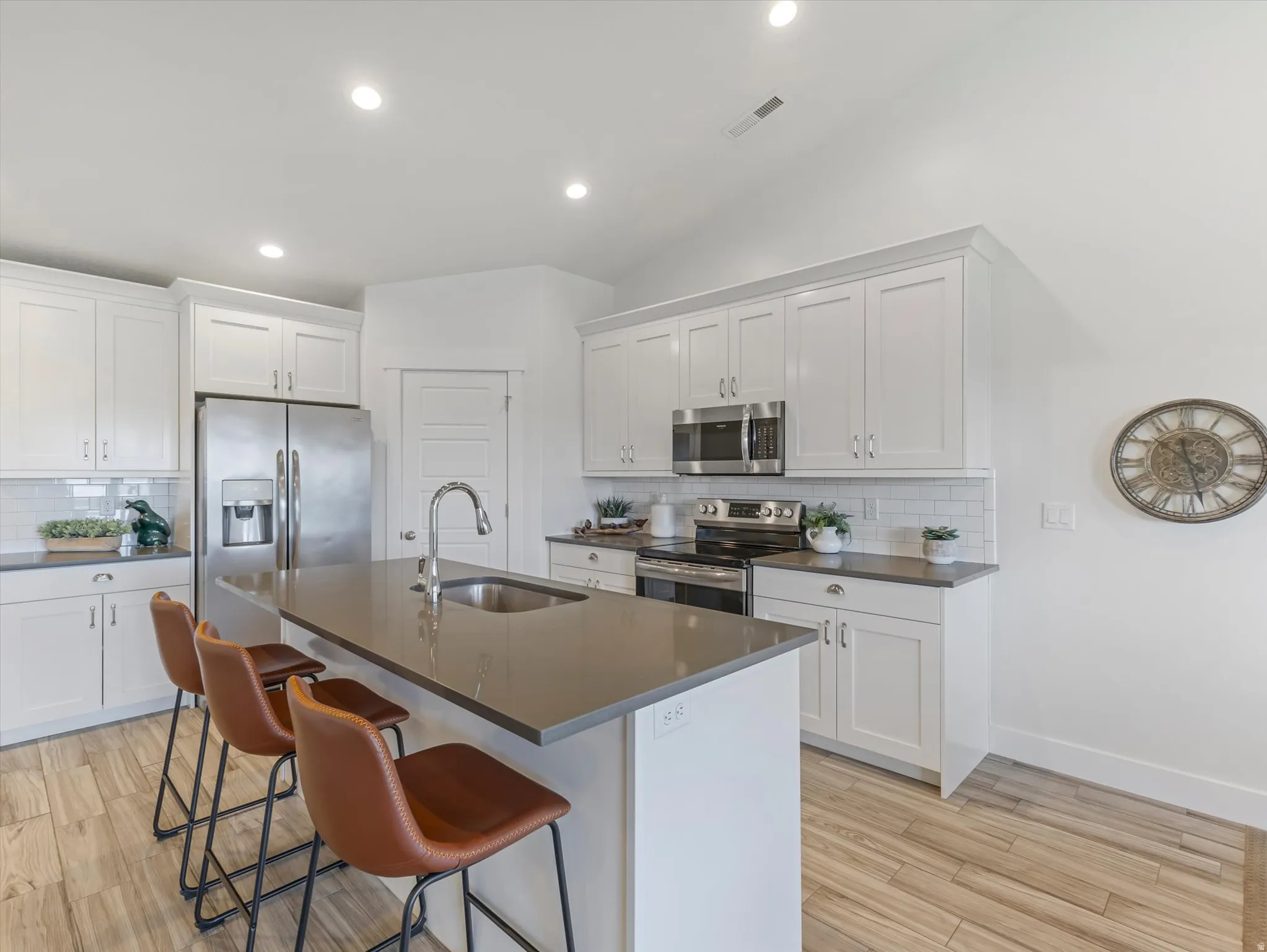 Modern kitchen featuring an island with an undermount sink, stainless steel appliances, white shaker-style cabinetry, subway tile backsplash, and wood-finish flooring