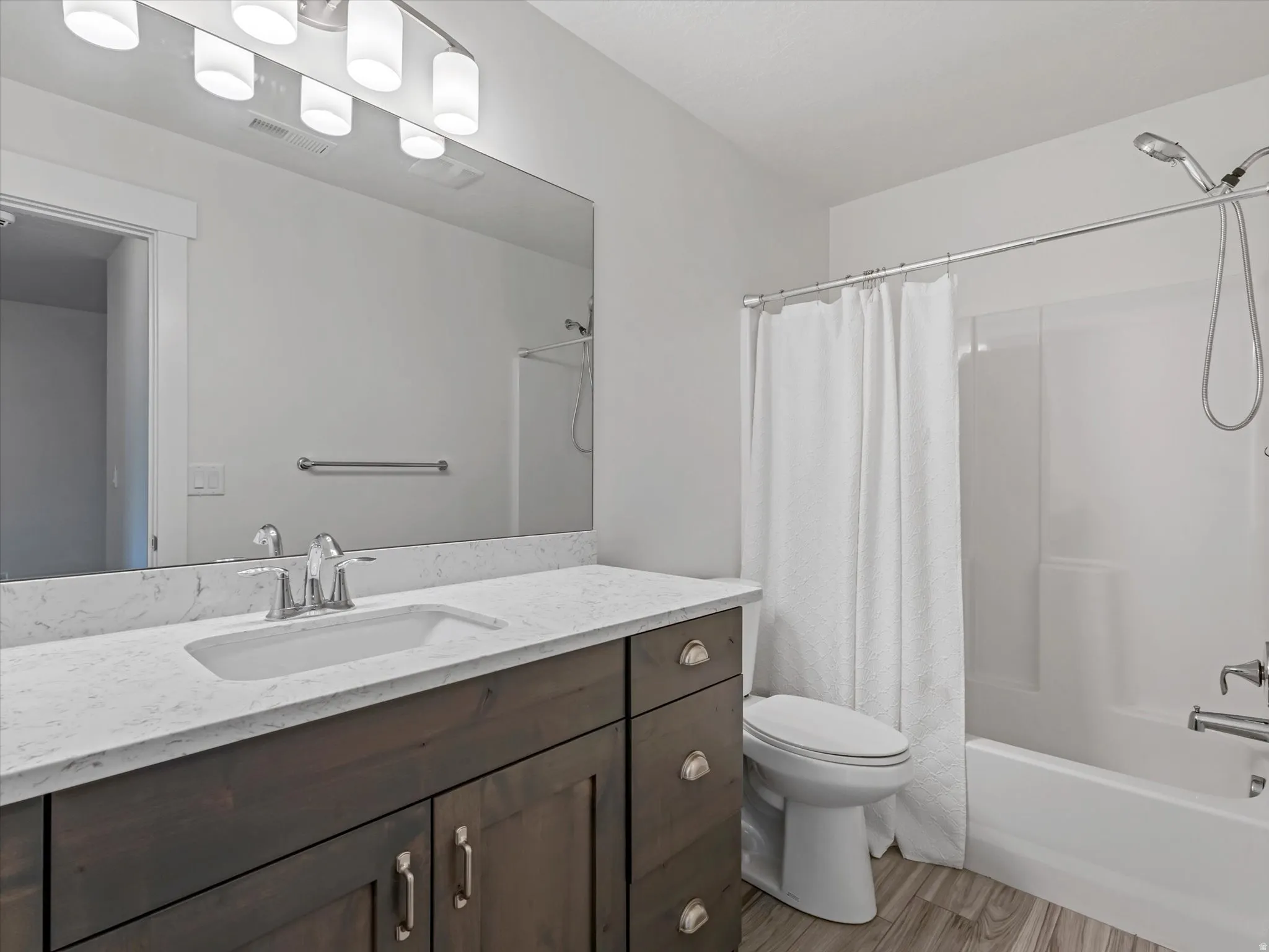 Bathroom featuring a wood-finish vanity with an integrated sink, a solid surface countertop, a large wall-mounted mirror, and a tub/shower combination