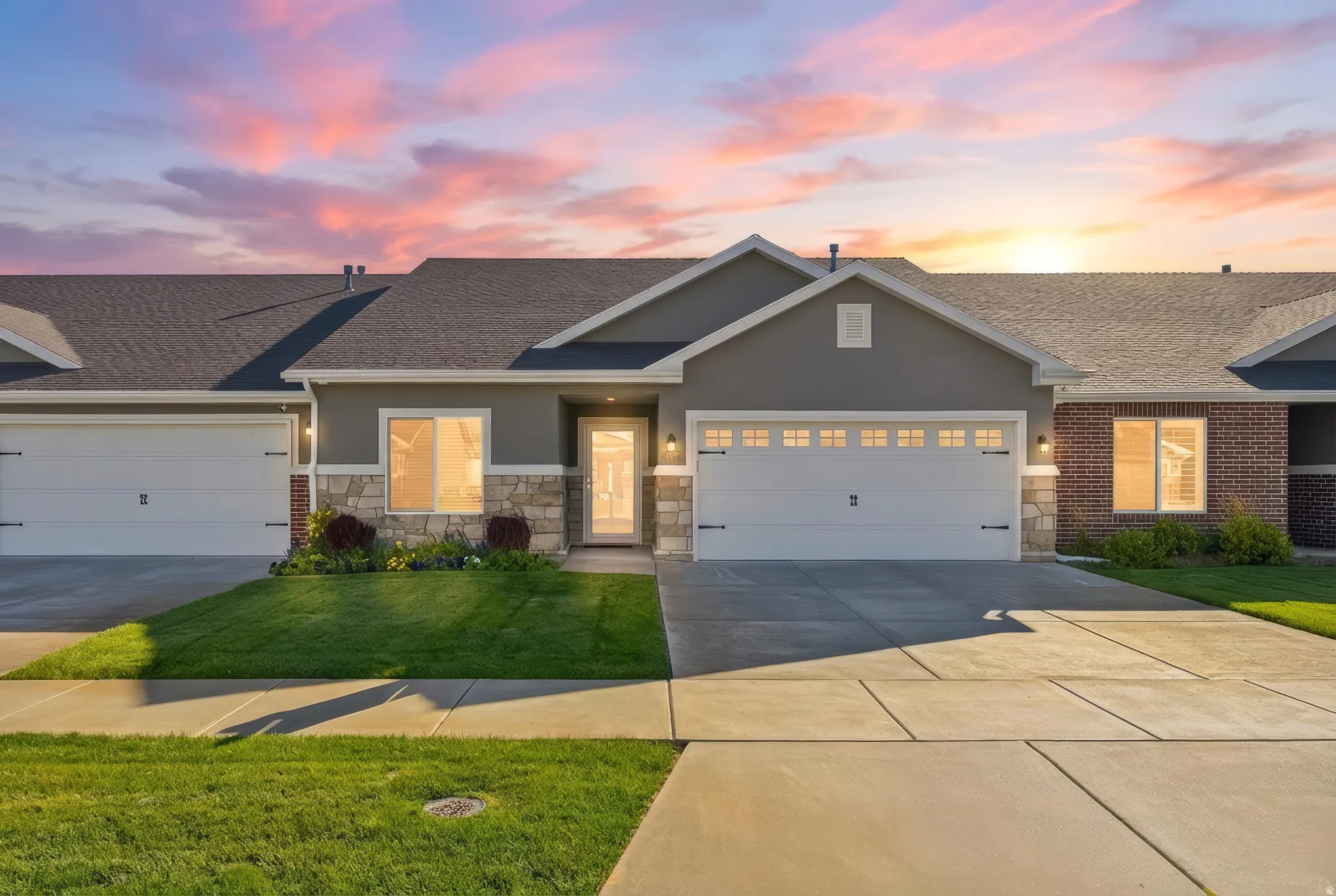 Modern ranch-style home featuring a two-car garage, stone facade accents, a dark shingle roof, concrete driveway, and a manicured lawn