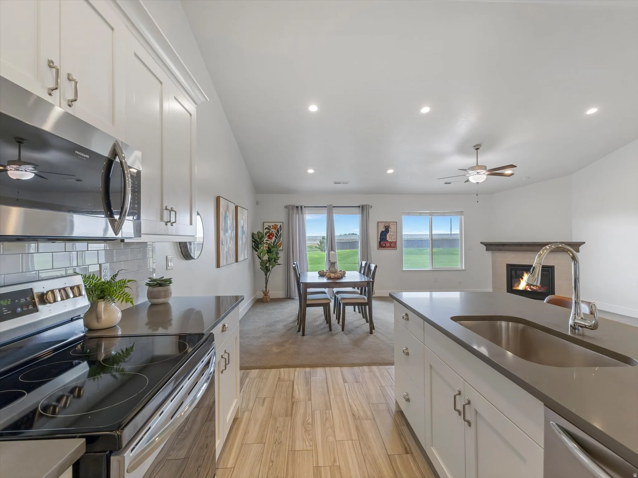 Open-concept living area featuring a kitchen island with an undermount sink, stainless steel appliances, white cabinetry, a subway tile backsplash, and a fireplace in the background