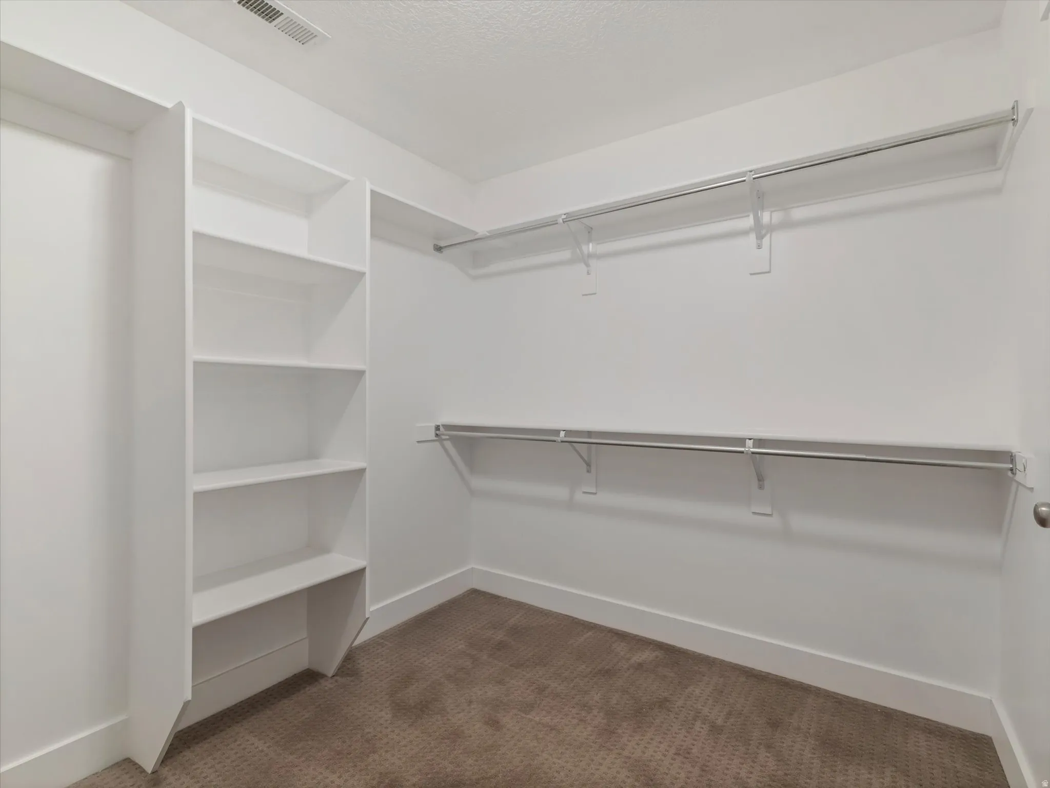 Walk-in closet featuring white built-in shelving, dual hanging rods, white baseboards, and textured carpeting