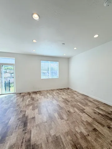 Spacious room featuring wood-finish flooring, recessed lighting, and white baseboards