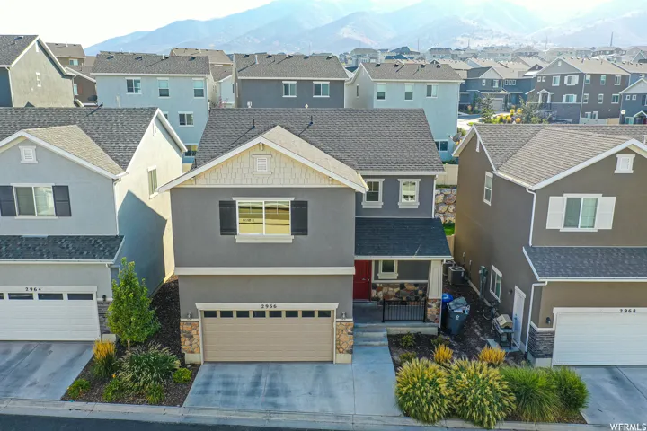 Contemporary two-story residence with a two-car garage, stone façade accents, covered entry porch, and mature landscaping