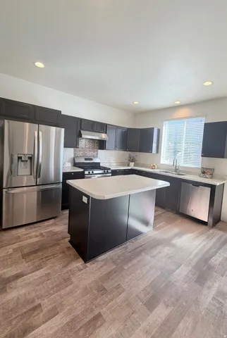 Modern kitchen featuring dark cabinetry, stainless steel appliances, a center island with light countertops, wood-finish flooring, and recessed lighting