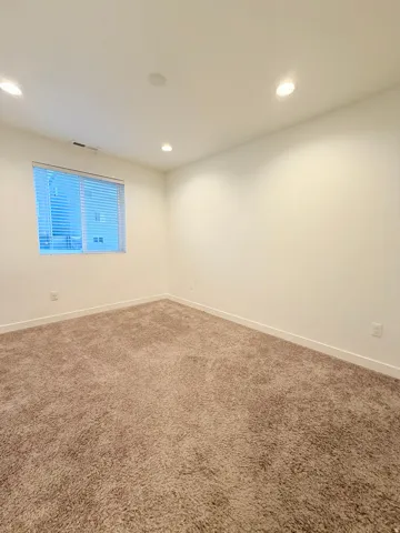 Carpeted interior space featuring white walls, recessed ceiling lighting, and a window with blinds and closet