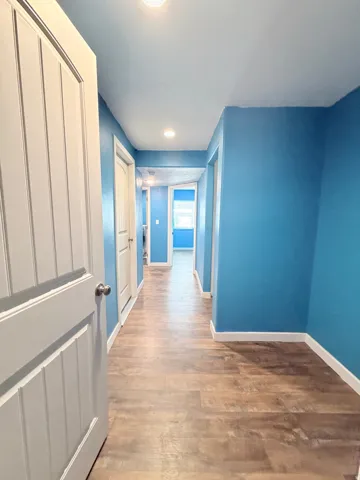 Hallway featuring wood-finish flooring, recessed lighting, and bright blue walls