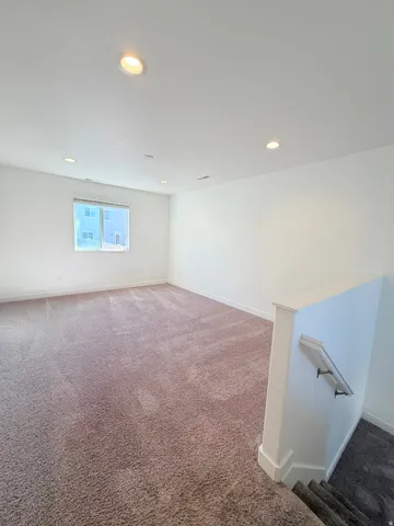 Spacious room featuring neutral carpeting, white walls, recessed lighting, and a large window with white trim