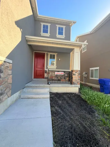 Stucco exterior featuring a covered porch with stone-clad columns and a bright red entry door