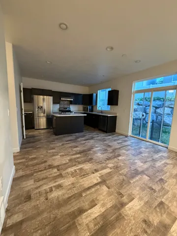 Open-concept kitchen and living area featuring wood-finish flooring, dark cabinetry, stainless steel appliances, and recessed lighting