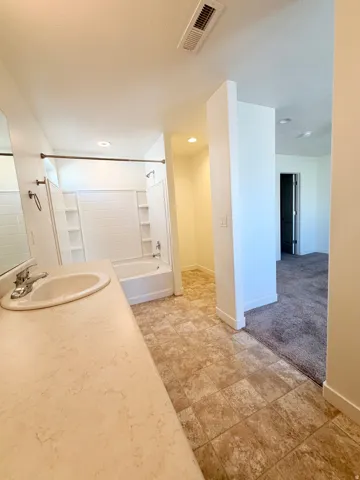 Master bedroom featuring a single-sink vanity with an integrated countertop, a white bathtub with a tiled surround, and patterned vinyl flooring
