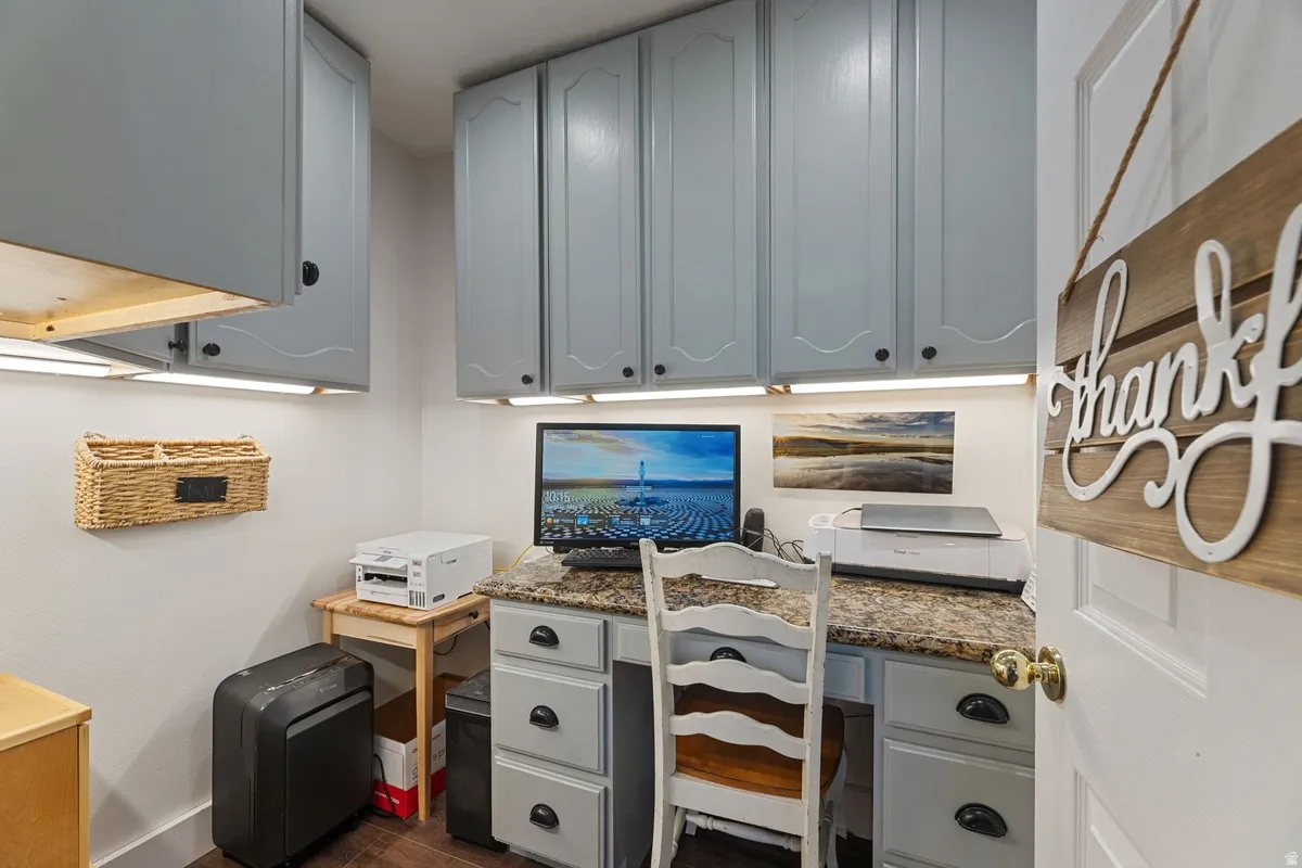 Dedicated workspace featuring built-in cabinetry with under-cabinet lighting, a built-in desk with a stone-finish countertop, and durable wood-finish flooring