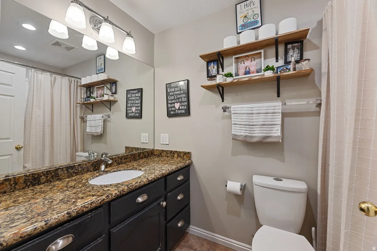 Bathroom featuring a vanity with a mottled countertop, an undermount sink, and dark cabinetry with silver-toned hardware