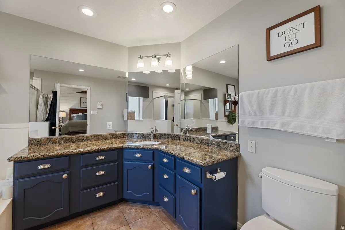 Bathroom featuring a corner vanity with a granite countertop, blue cabinetry, dual sinks, and extensive mirror coverage