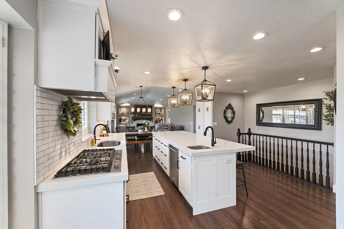 Spacious kitchen featuring an expansive island with an undermount sink, a gas cooktop with a subway tile backsplash, white cabinetry, and recessed lighting