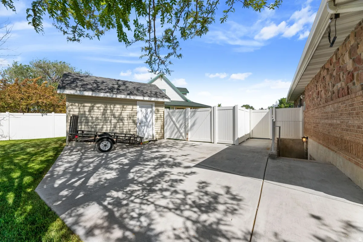 Paved concrete patio featuring a detached storage shed, white privacy fencing, and exterior wall lighting