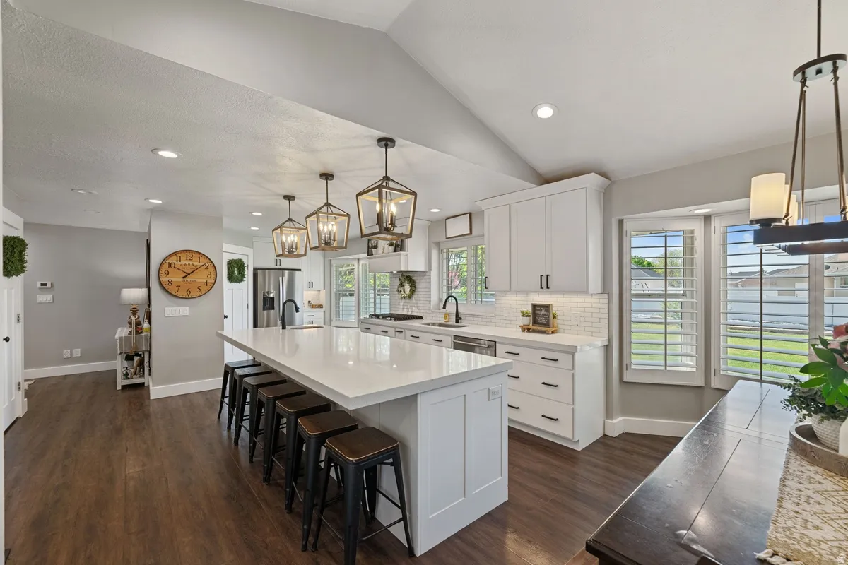 Spacious kitchen featuring an extended island with seating, white shaker cabinetry, subway tile backsplash, and wood-finish flooring