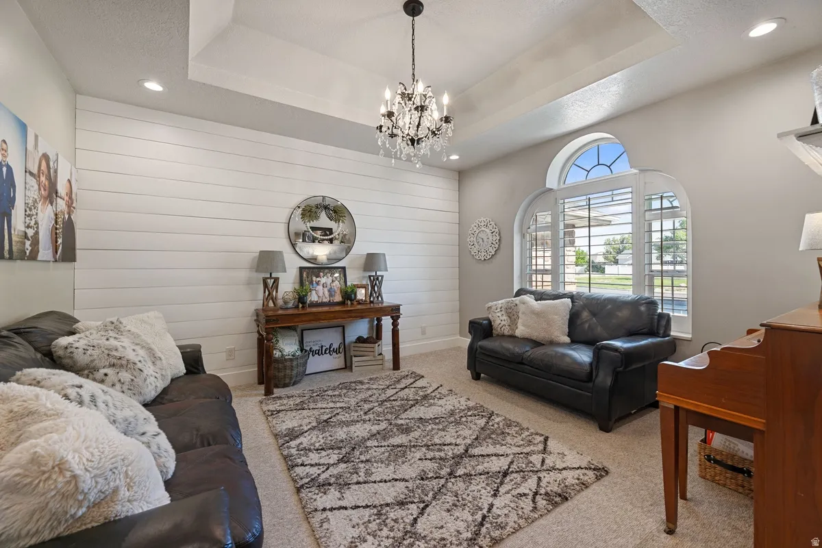 Living area featuring shiplap accent wall, tray ceiling, recessed lighting, and an arched window with plantation shutters