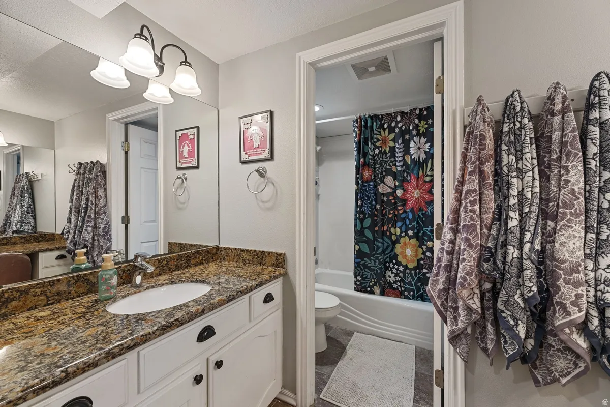 Bathroom featuring a vanity with a granite-style countertop, white cabinetry with dark hardware, an integrated sink, and a wall-mounted mirror