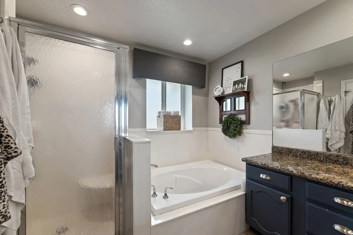 Bathroom featuring a built-in soaking tub, a separate shower with textured glass enclosure, recessed lighting, and a vanity with a granite-style countertop and dark cabinetry