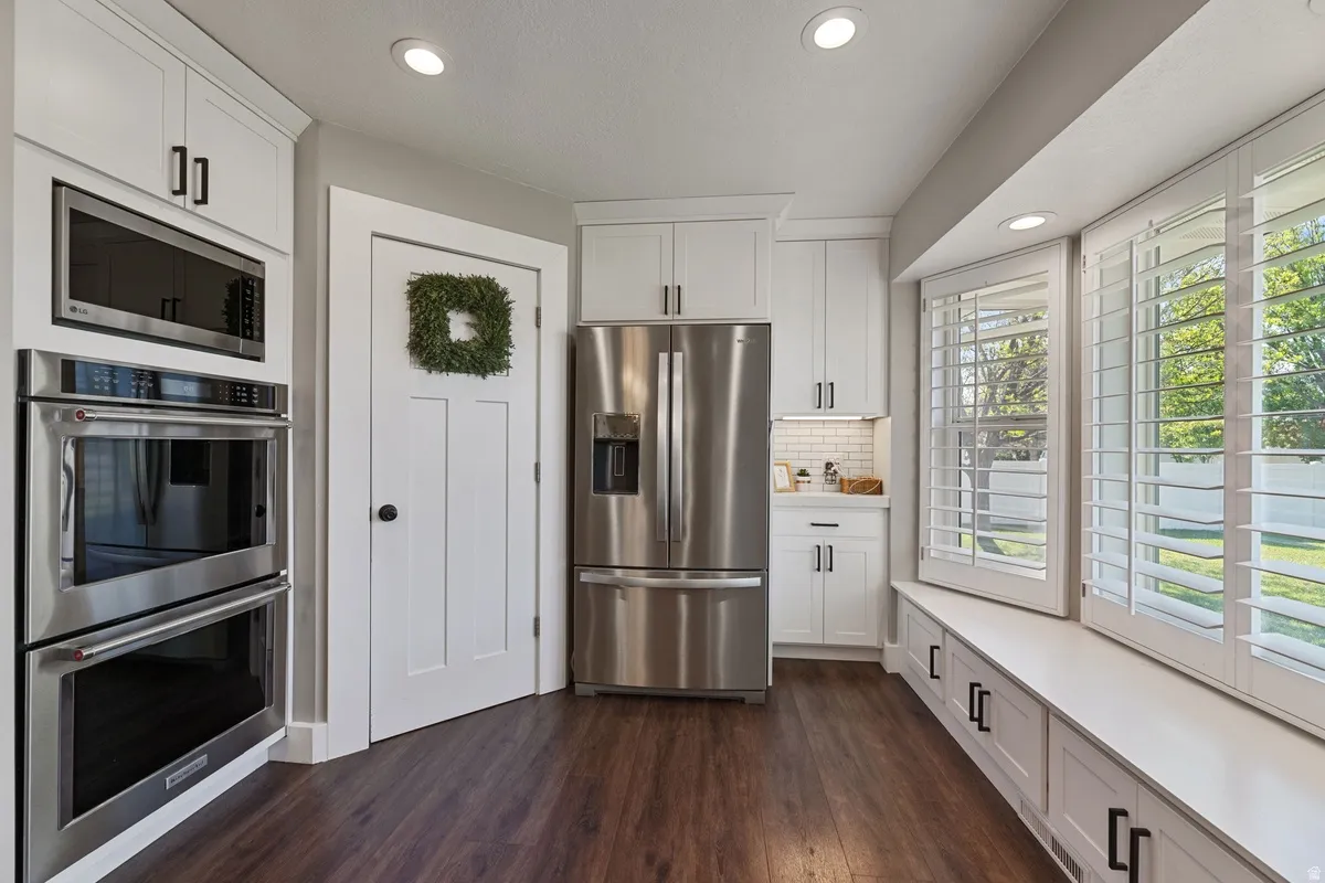Kitchen featuring stainless steel appliances, white cabinetry with dark hardware, recessed lighting, wood-finish flooring, and a window seat with integrated storage and plantation shutters