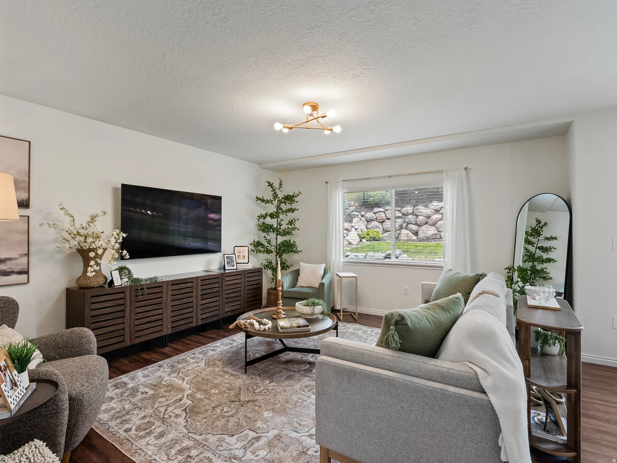 Spacious living area featuring wood-finish flooring, a contemporary light fixture, and a large window with white blinds
