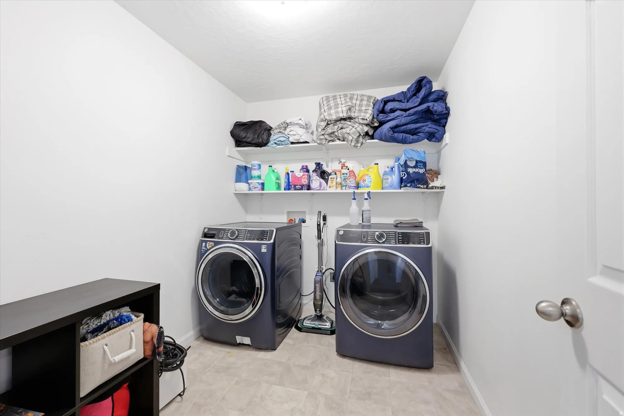 Dedicated laundry area featuring a light-toned flooring, white walls, and built-in shelving