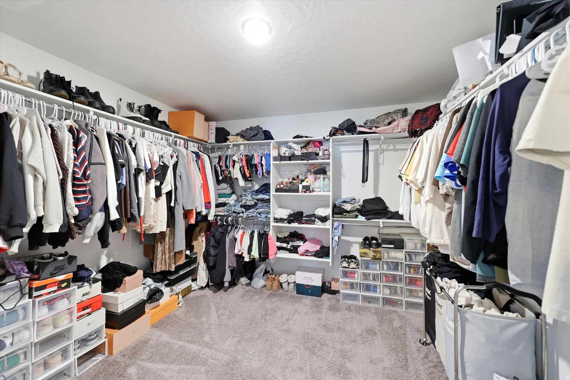 Spacious walk-in closet featuring extensive built-in shelving, multiple hanging rods, and neutral-toned carpeting in the primary bedroom