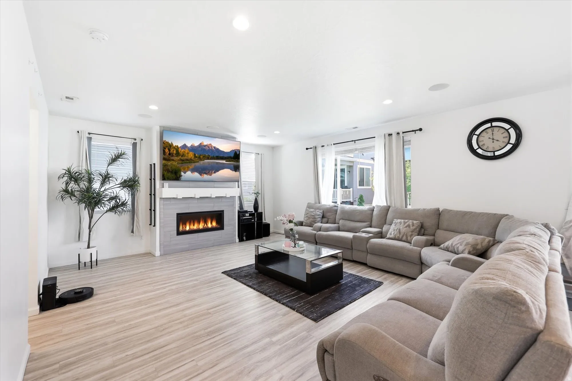 Spacious living area featuring light wood-finish flooring, a contemporary fireplace with a light-toned tile surround, and recessed ceiling lighting