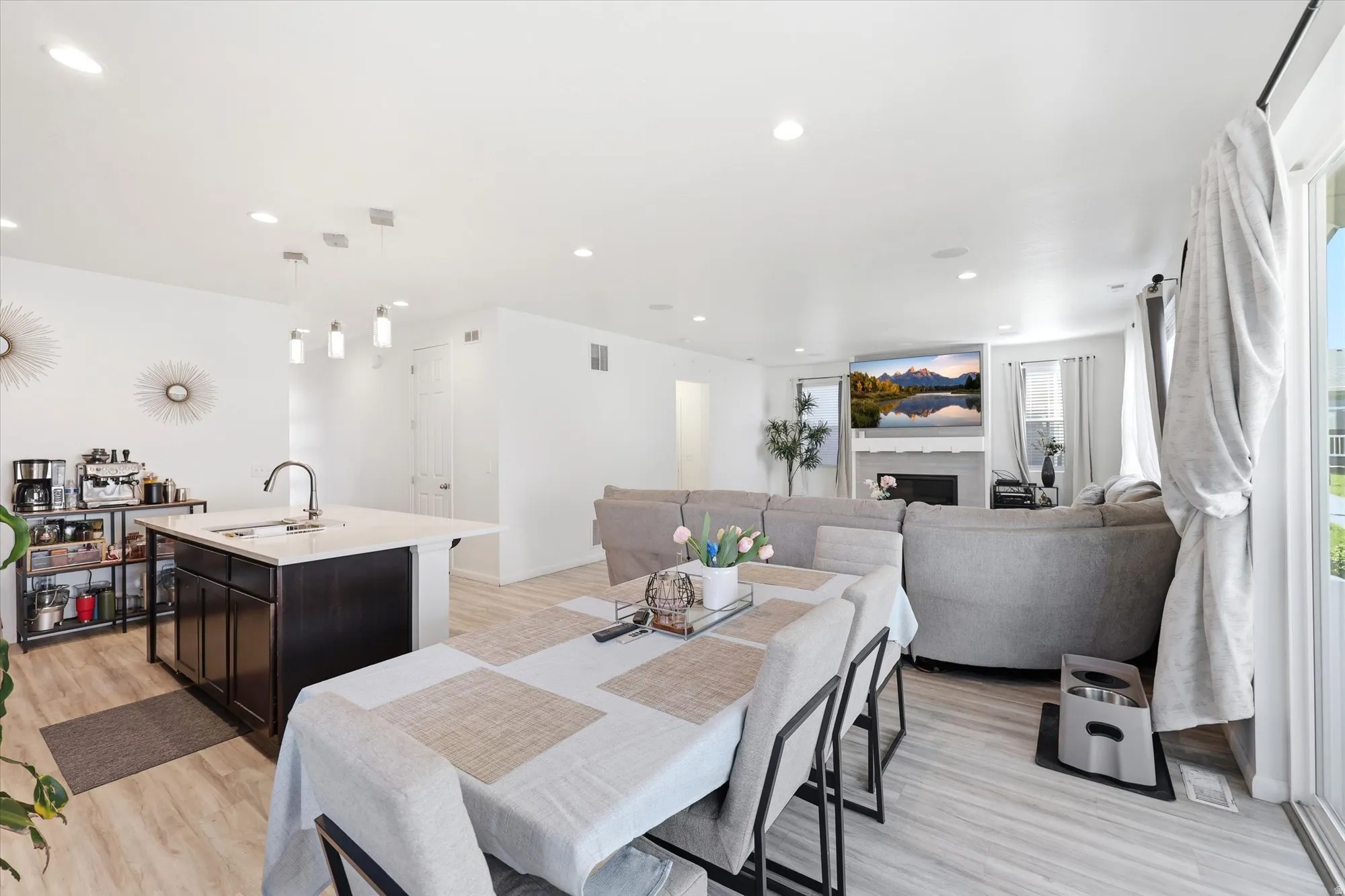 Open-concept living space featuring light wood-finish flooring, recessed lighting, and a kitchen island with a built-in sink and pendant lighting