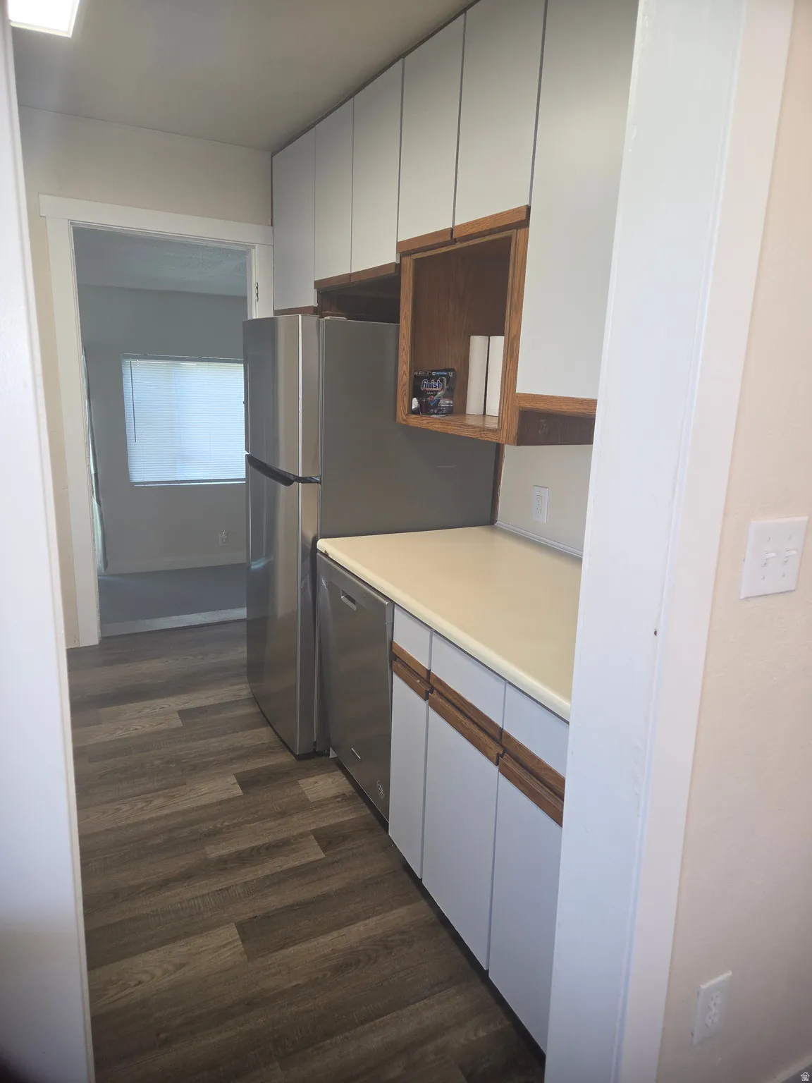 Galley kitchen featuring wood-finish flooring, stainless steel refrigerator, and integrated dishwasher