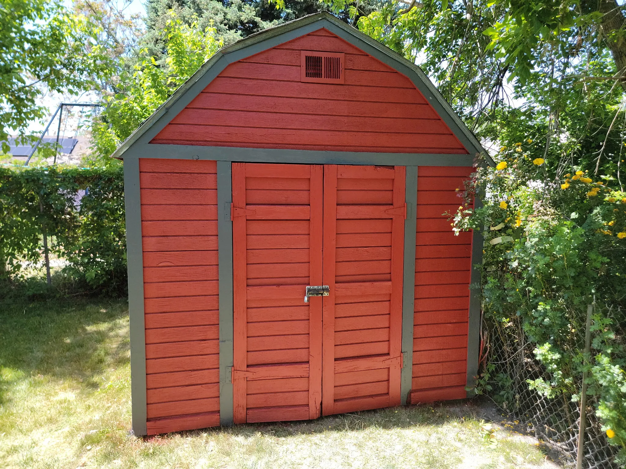 Red storage shed featuring a gambrel roof and double louvered doors