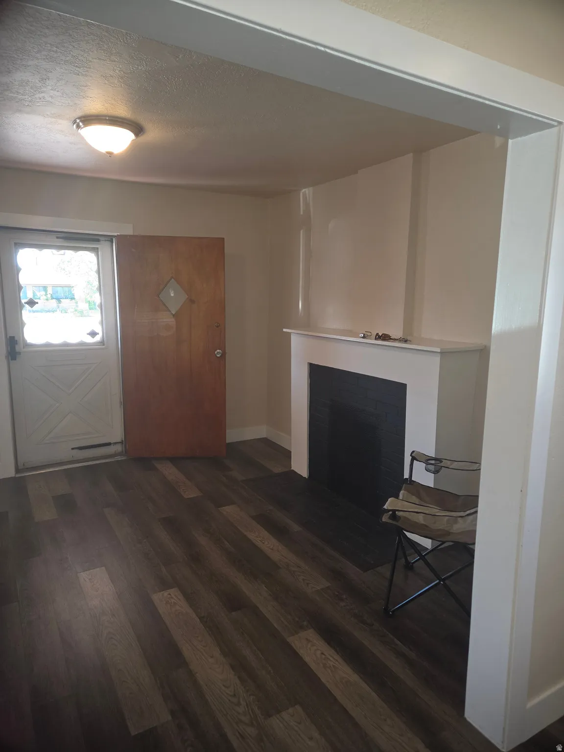 Entryway featuring wood-finish flooring, a white mantel, and a fireplace with a black insert