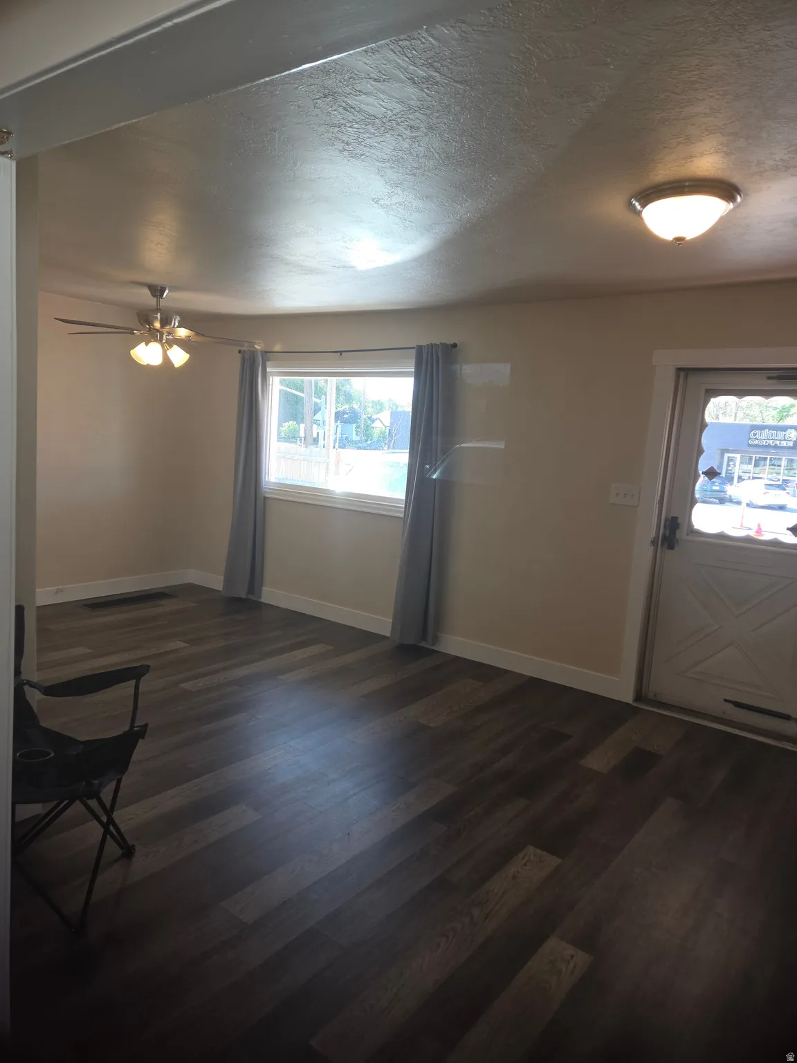 Living area featuring dark wood-finish flooring, a ceiling fan with integrated lighting, and a front entry door with an X-panel design