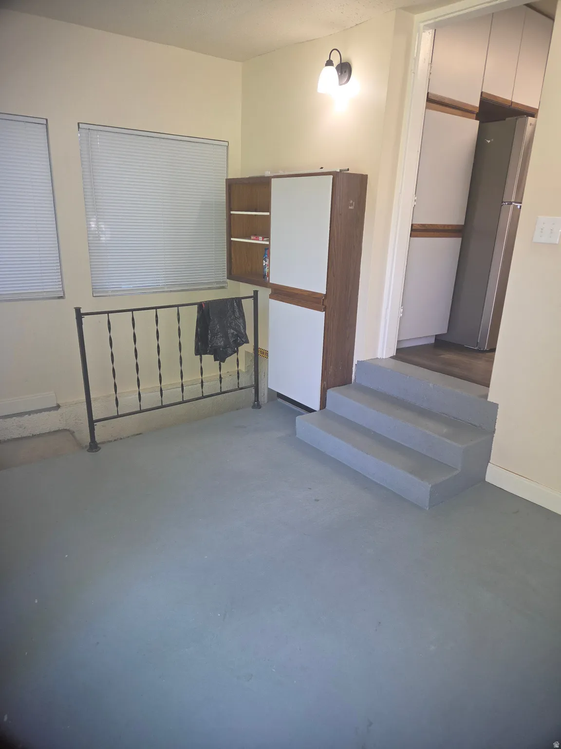 Multi-purpose room featuring two windows with horizontal blinds, a black wrought iron railing, and a built-in cabinetry unit with wood-finish and white panels