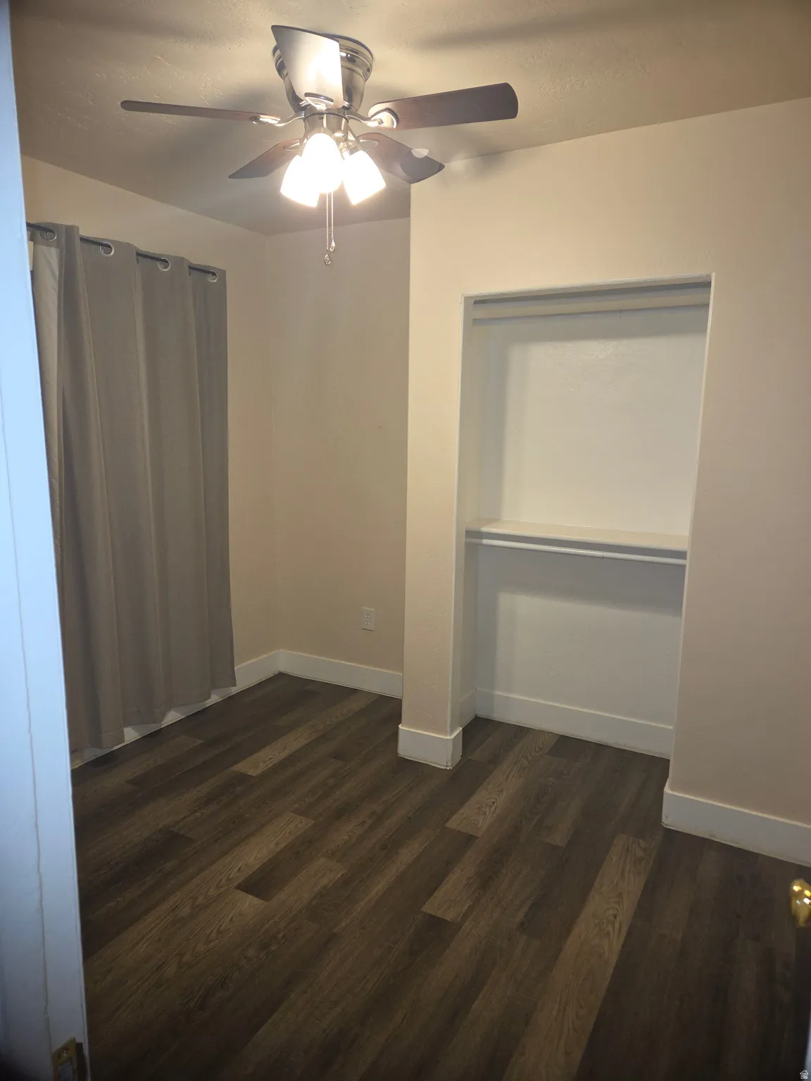 Room featuring wood-finish flooring, a built-in closet with shelving, a ceiling fan with integrated lighting, and neutral wall tones
