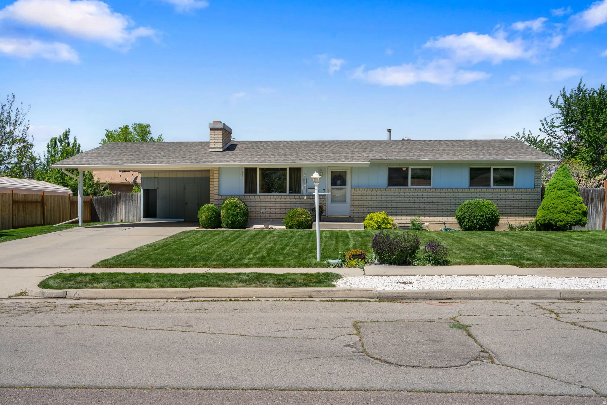 Ranch-style residence featuring a carport, brick and siding exterior, front lawn, and mature landscaping